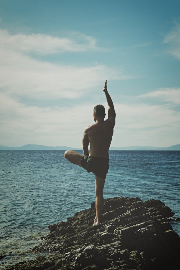 Back view of a man practicing yoga on a rocky seashore. Embracing peace, meditation, and nature. Balance